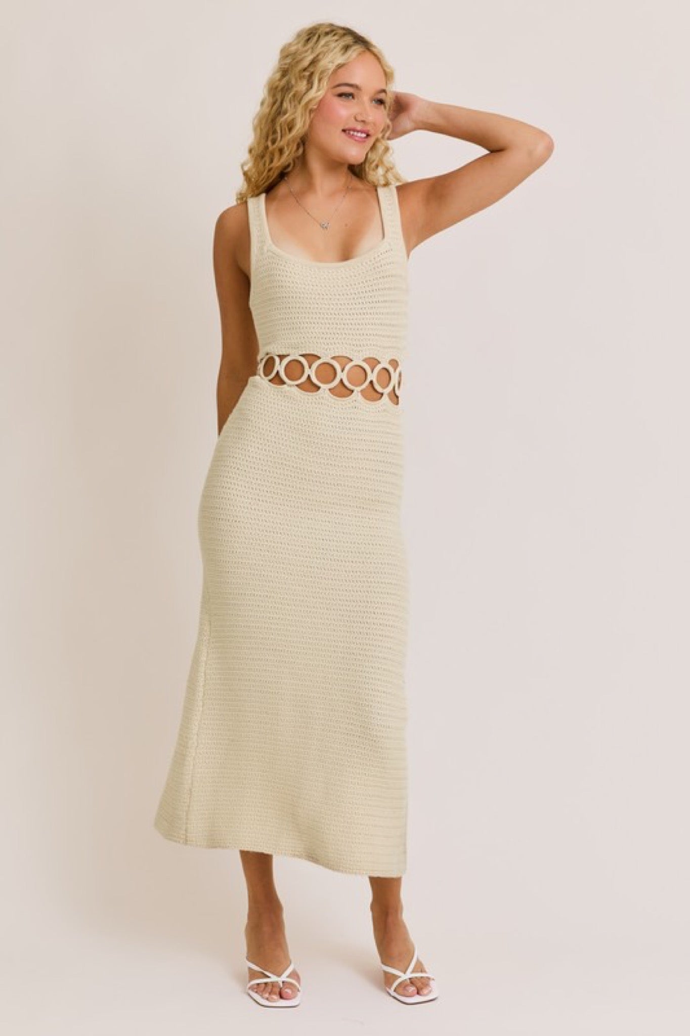 Woman wearing a light-colored dress with cut-out design on a plain background