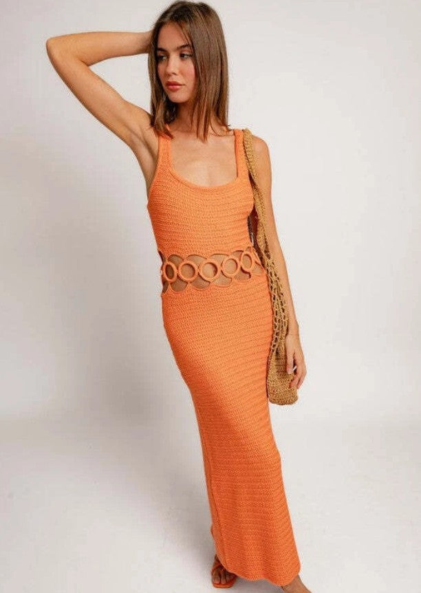 Woman wearing an orange dress with a belt and holding a straw bag on a white background