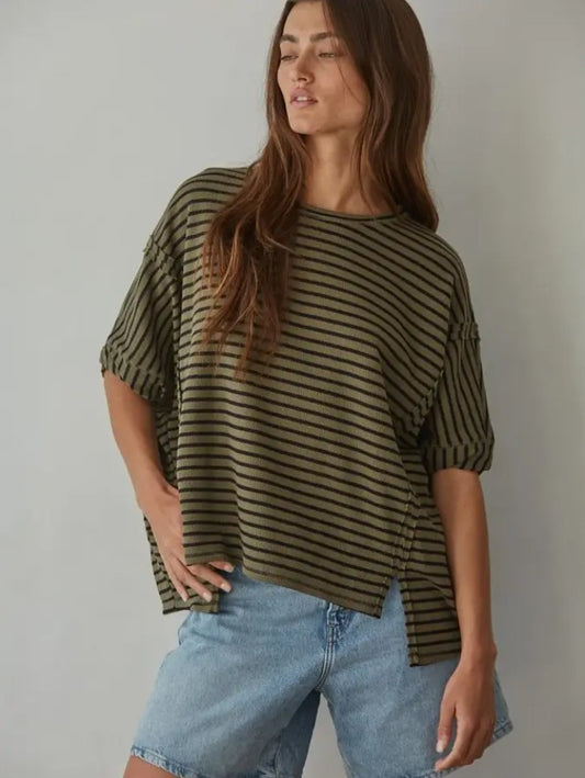 Woman wearing a green and black striped shirt with light blue jeans against a plain background