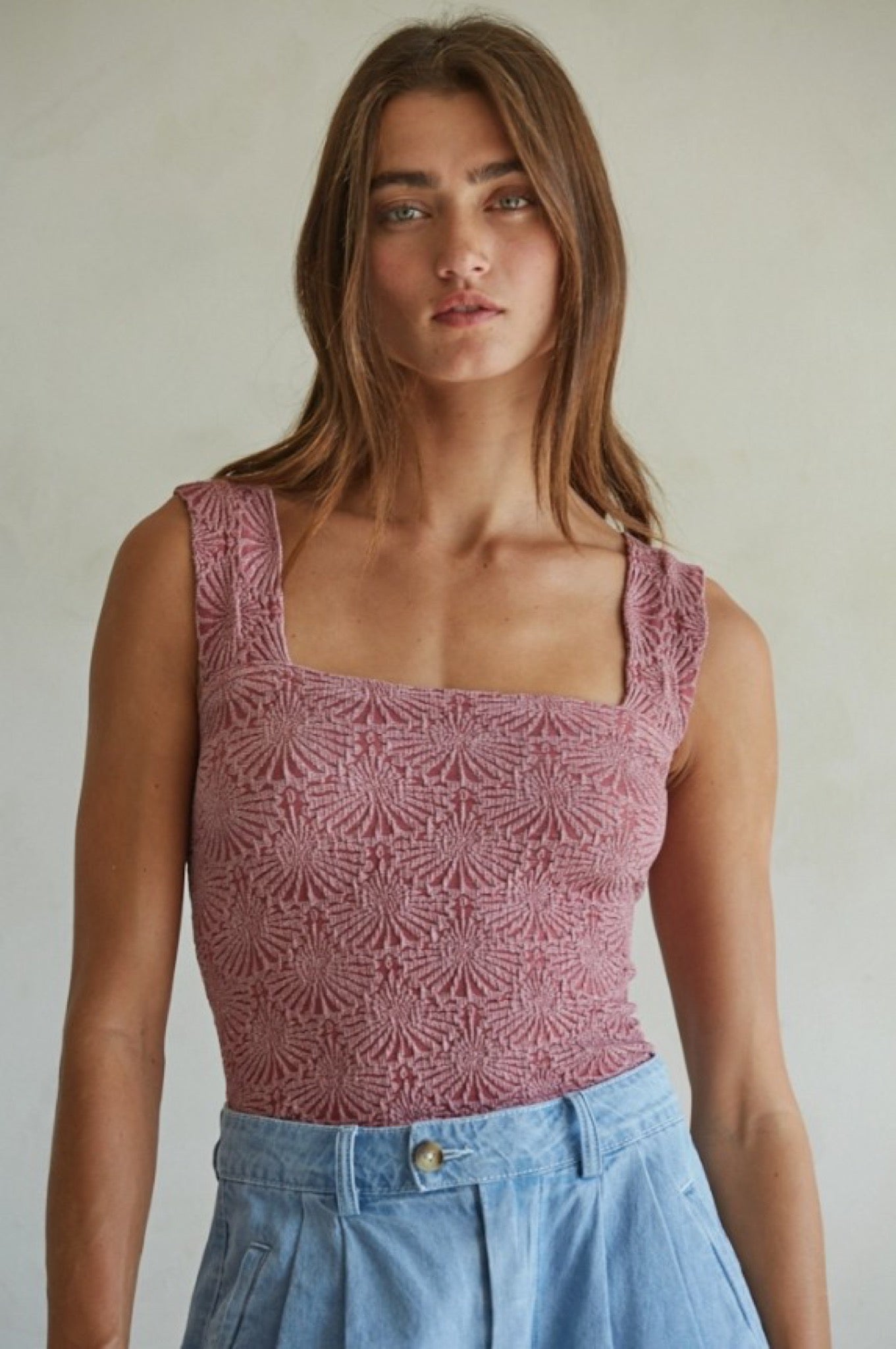 Woman wearing a patterned pink top and blue jeans against a plain background