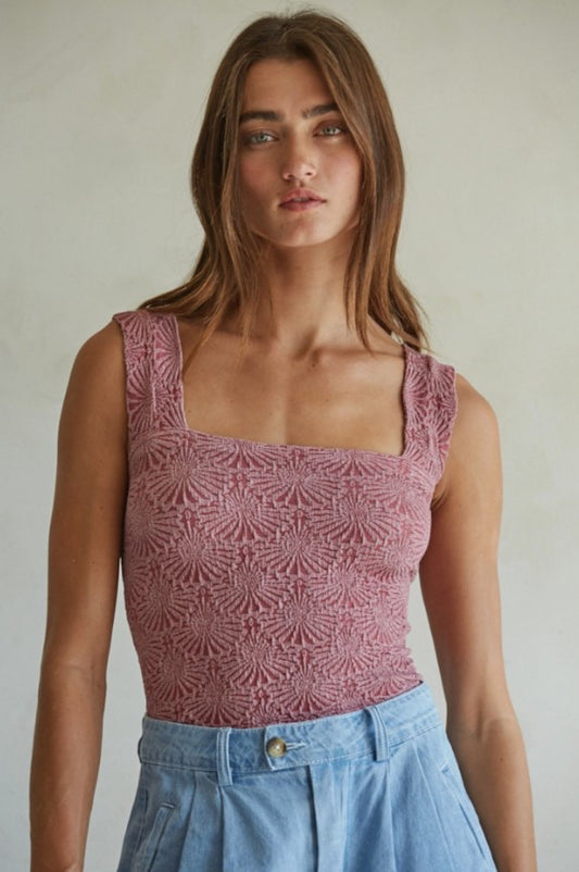 Woman wearing a patterned pink top and blue jeans against a plain background