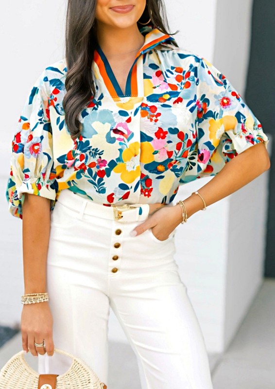 Woman wearing a colorful floral blouse and white pants indoors.