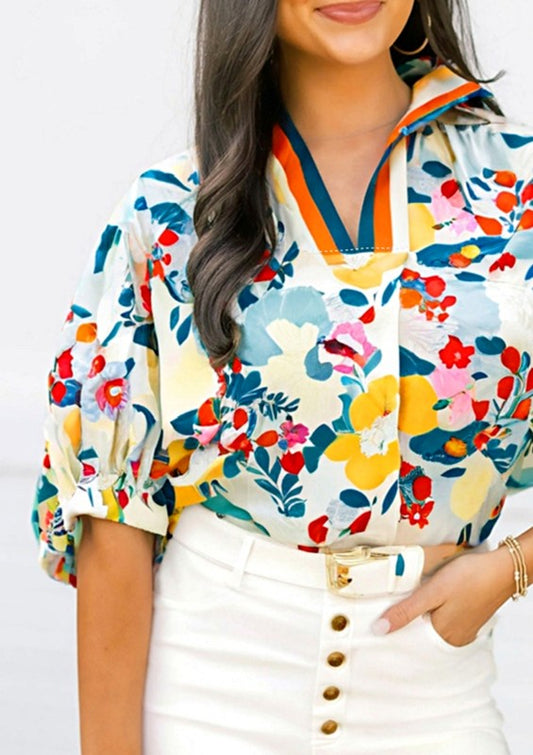 Woman wearing a colorful floral blouse with a white skirt on a plain background