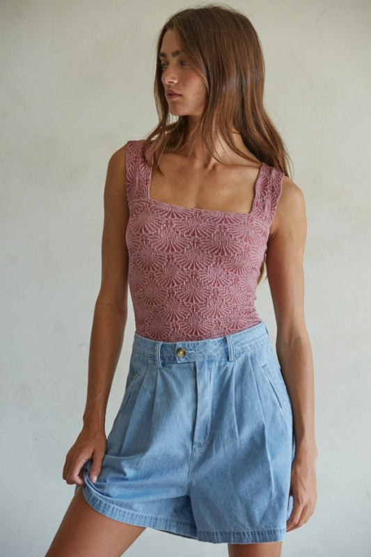 Woman wearing a pink lace top and blue shorts against a plain background