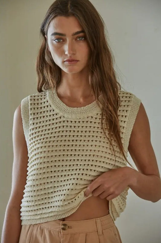 Woman wearing a beige crochet top against a plain background
