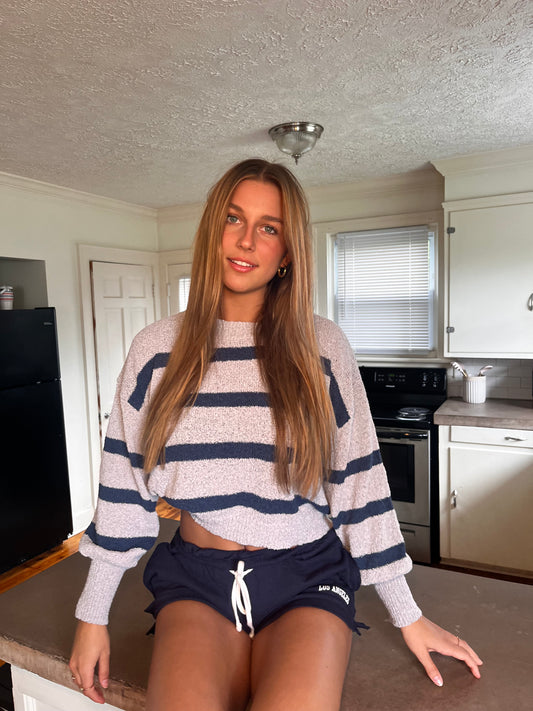 Kaia wearing a striped sweater and shorts in a kitchen setting