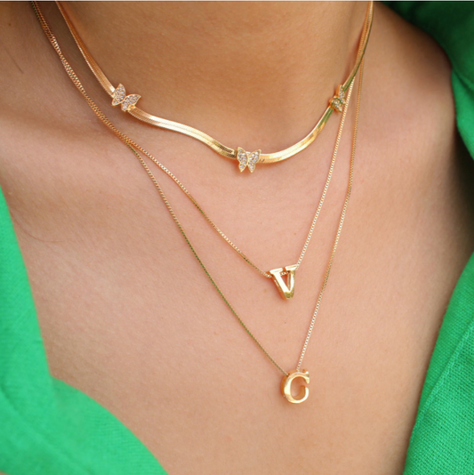 Gold necklaces with butterfly and letter 'V' and 'G' pendants on a person wearing a green top.